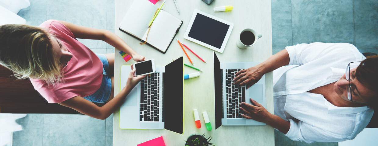 Two people sitting at conference room table while working on laptops.