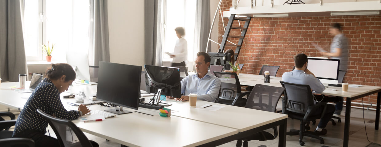 Busy office space with employees working at desk and walking around.