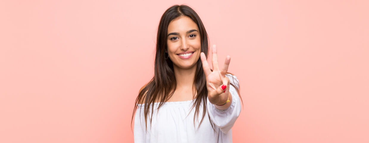 Young woman smiling and hold up three fingers.