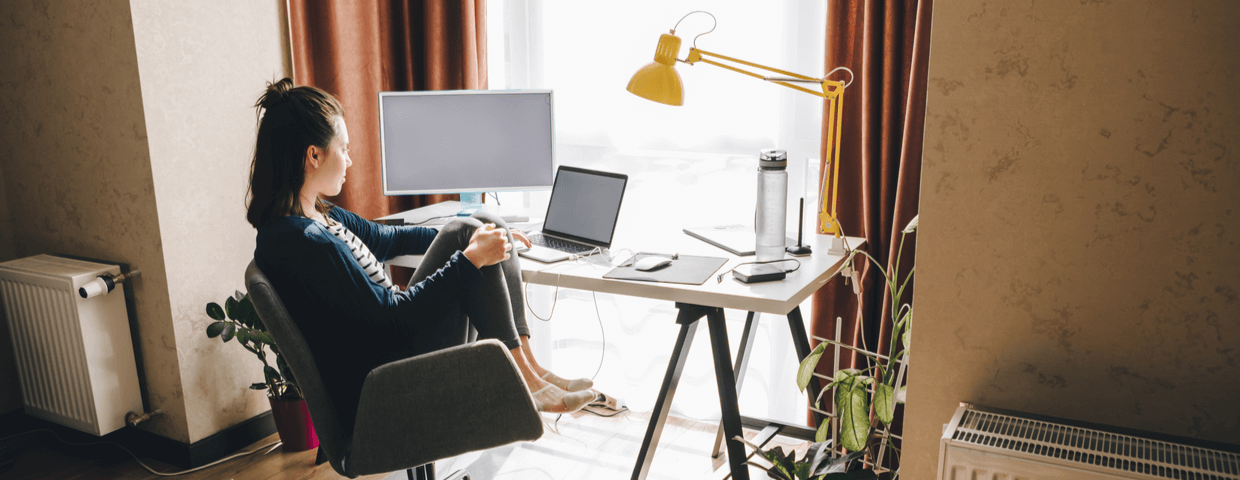 Woman working from home, sitting at home desk and looking out window.