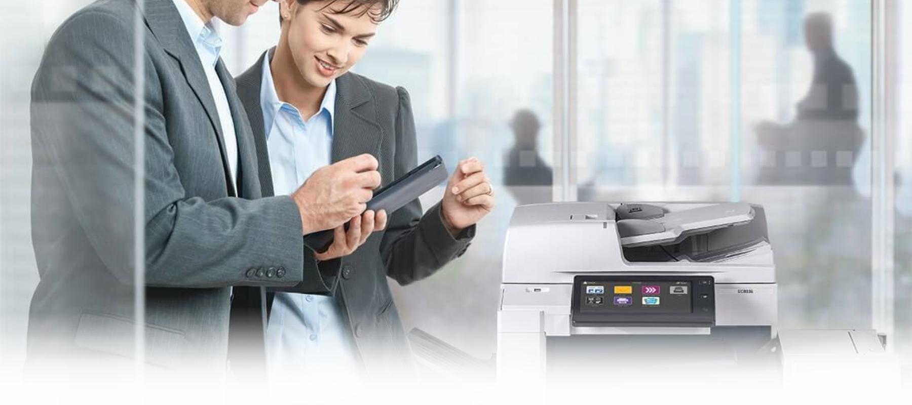 Man and woman standing in an office over a printer or mfp