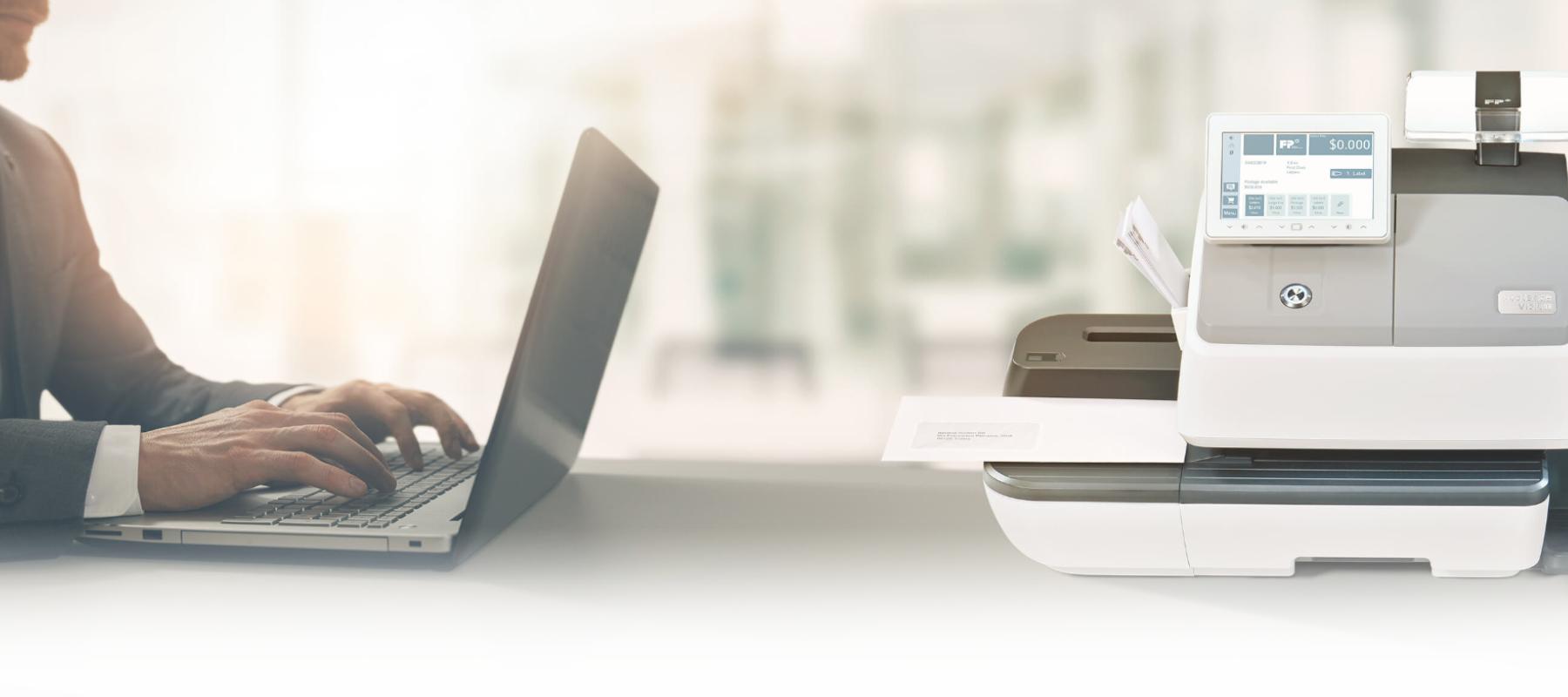 Close up of man working on laptop with a mailing solution printer on the desk