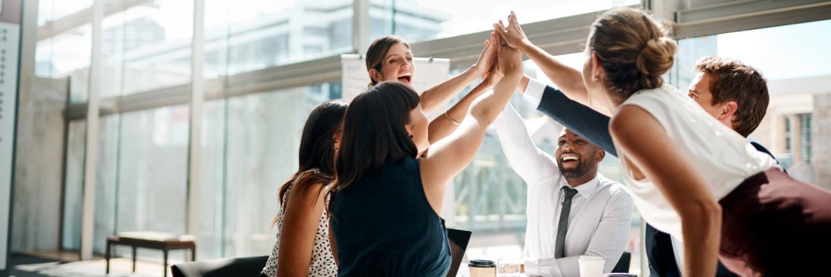 Group of happy employees leaning over a desk or conference table giving each other a high five