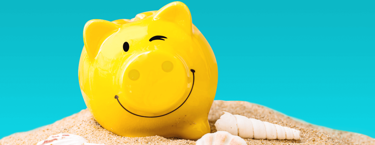 Yellow smiling and winking piggy bank on top of sand and sea shells with blue background