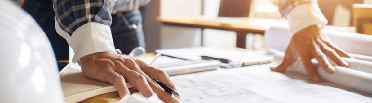 close up of an architect or engineers hands sitting on a blueprint with drawing tools on the desk