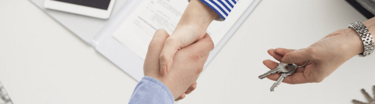 realtor and client shaking hands, keys in hand and contract on the desk below