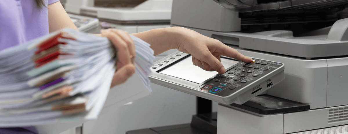 Woman holding stack of papers, using office equipment.